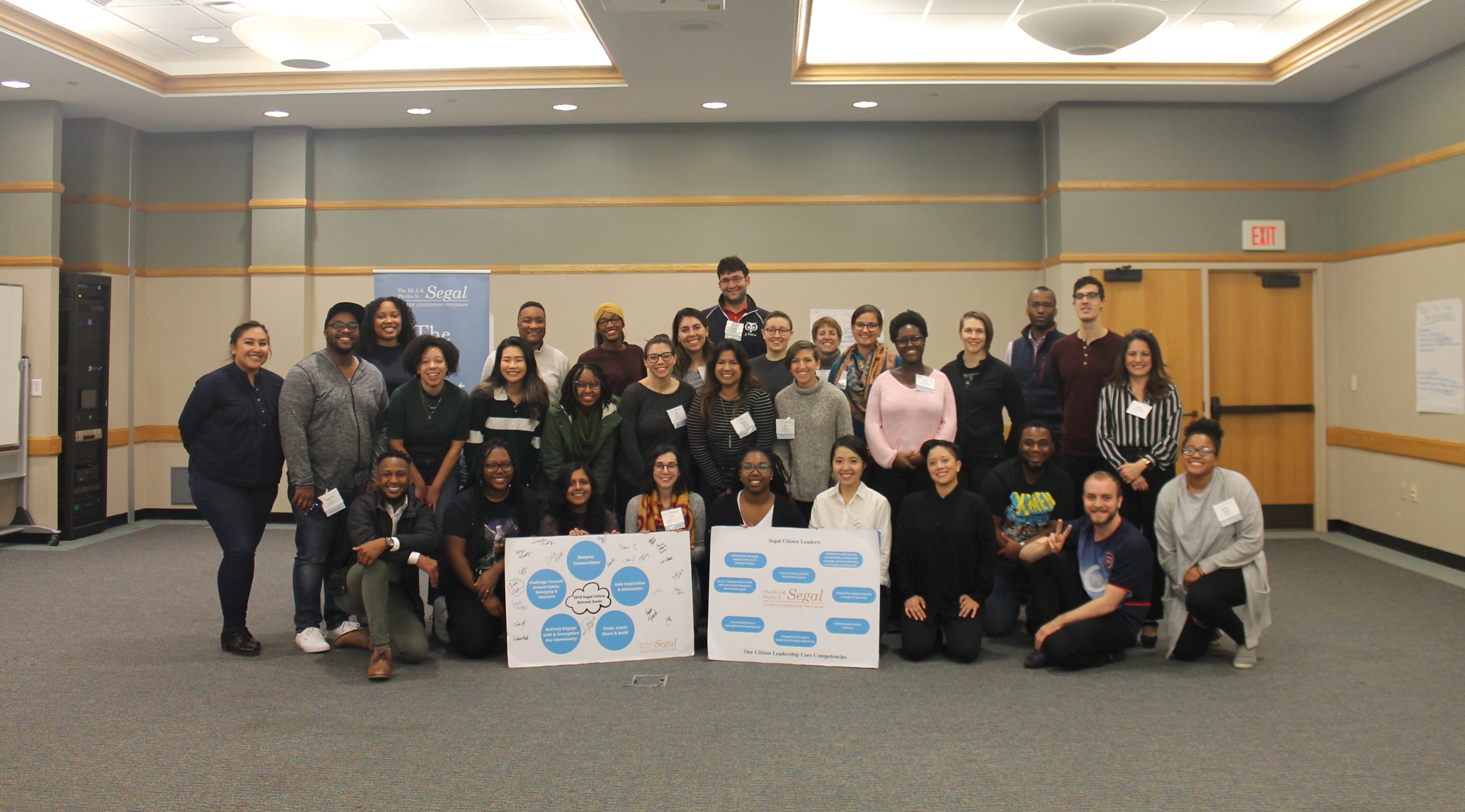 Segal Fellows posing for group photo with retreat goals and welcome board at Segal Fellow Retreat